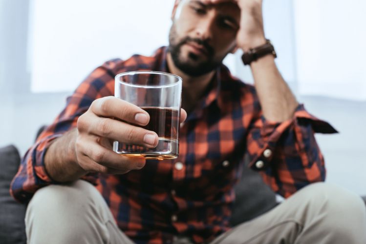 Man struggling with alcohol addiction, holding a glass, seeking support – focus on how to help someone with alcohol addiction in Tennessee.