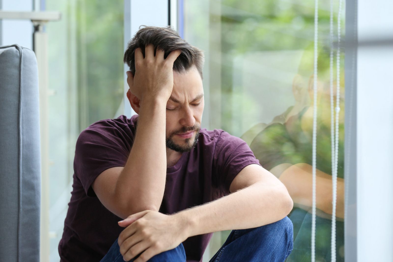 Man sitting by a window appearing distressed, representing the struggles of opioid addiction, emphasizing the importance of Fentanyl Rehab in Nashville, TN for recovery.